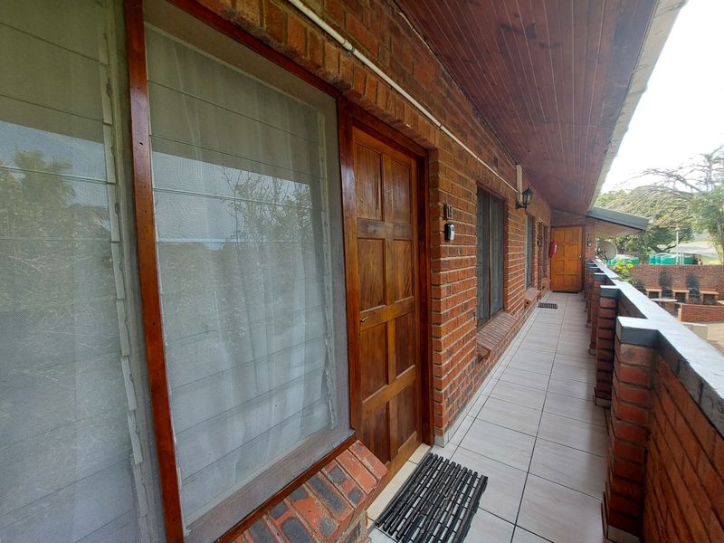 A covered exterior balcony featuring exposed brick walls, tiled flooring, and a timber-panelled ceiling, providing access to the apartment entrance.