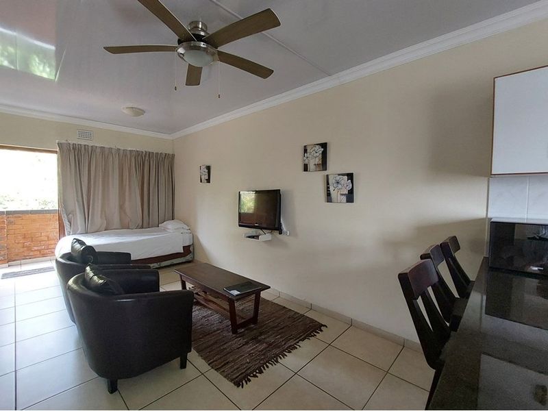 Open-plan living area featuring tiled flooring, a ceiling fan, and an integrated kitchen counter, with direct access to an outdoor balcony.