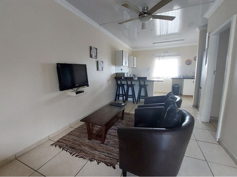 Open-plan living and kitchen area featuring tiled flooring, a ceiling fan, and a functional kitchen layout with a breakfast bar.
