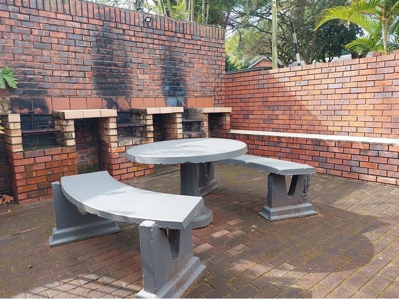 Outdoor patio area featuring a built-in brick braai, paved flooring, and a fixed concrete seating area, ideal for outdoor entertaining.