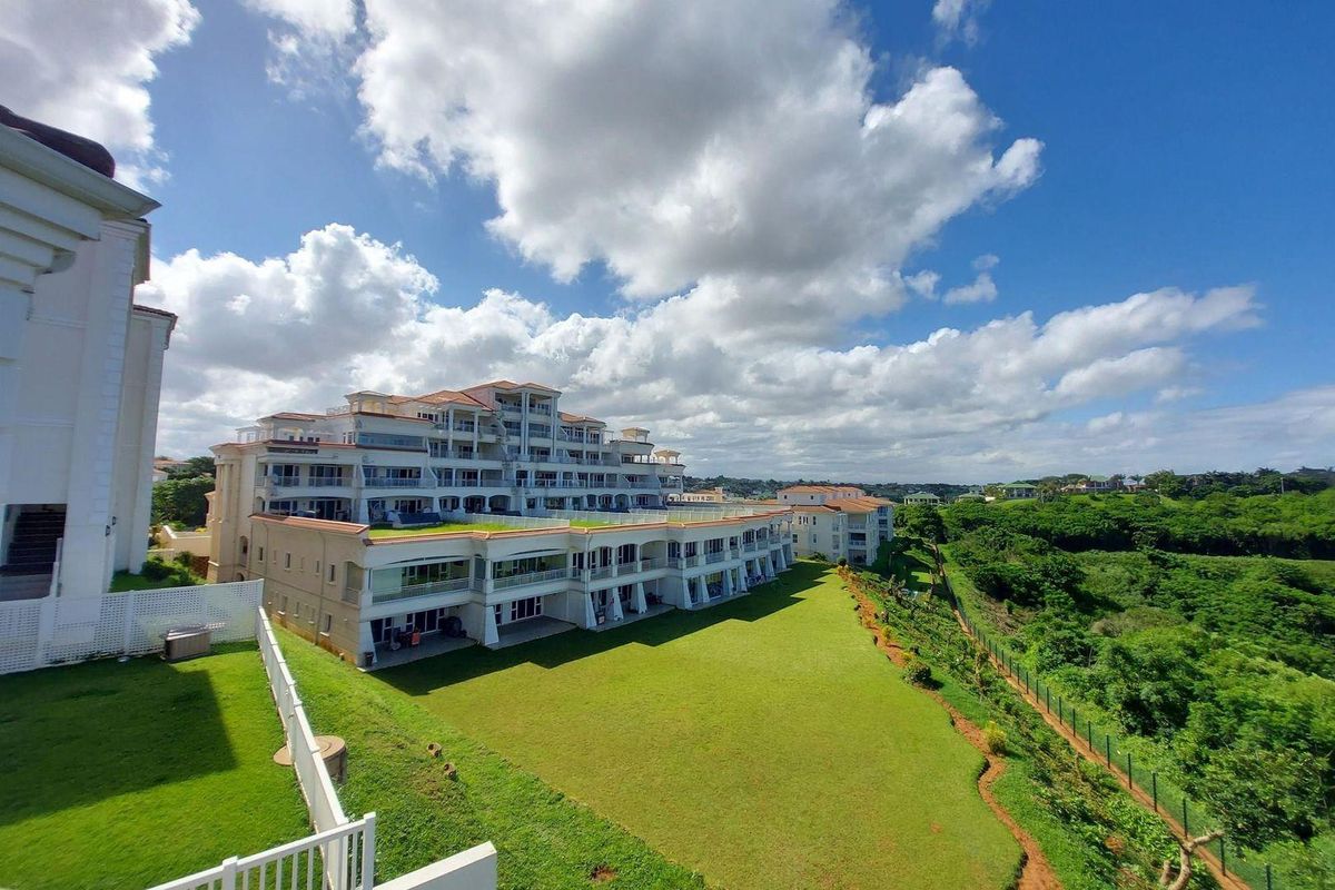 An elevated aerial view of a multi-story residential townhouse complex featuring landscaped lawns, terraced balconies, and scenic surrounding greenery.