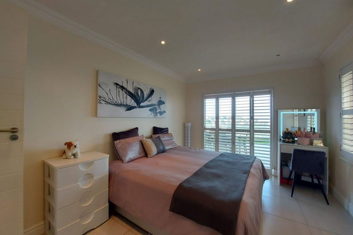 A well-maintained bedroom featuring tiled flooring, recessed ceiling lighting, and white plantation shutters opening to an outdoor area.