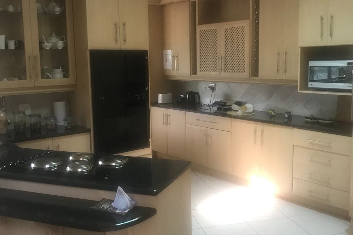 A spacious kitchen featuring built-in cabinetry, dark granite countertops, a central island with a cooktop, and tiled flooring.