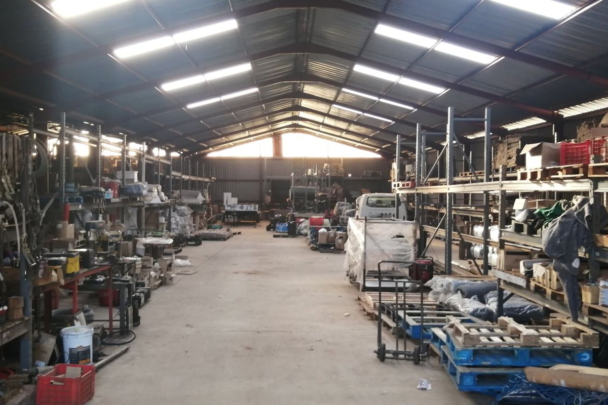 Large industrial-style farm shed featuring high-pitched corrugated metal roofing, skylights, and extensive heavy-duty steel racking systems for storage.