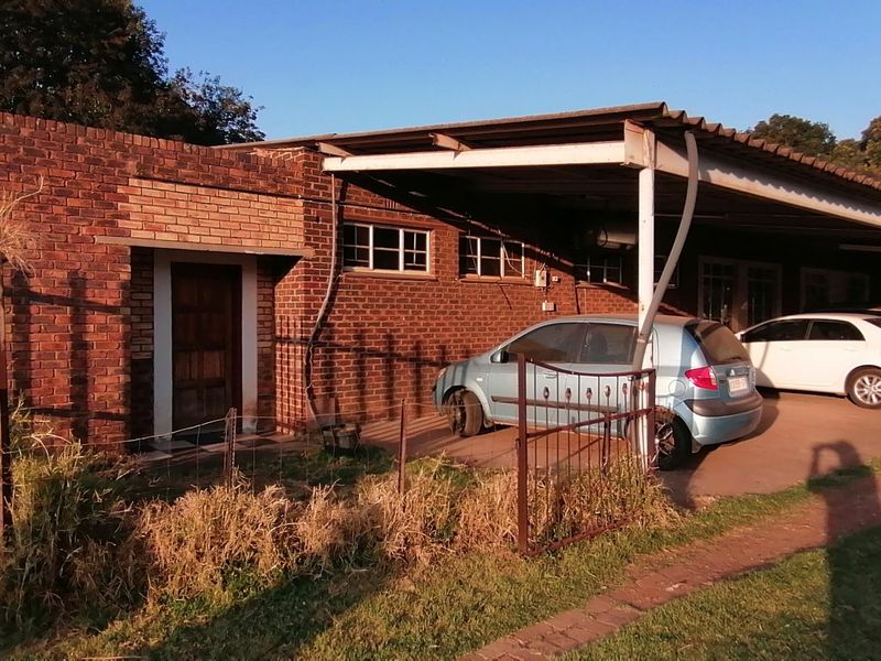 Exterior view of a brick farm building featuring a large attached carport area and basic metal fencing.