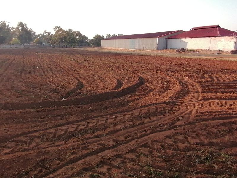Expansive tilled agricultural land on a farm property, featuring a large outbuilding with a red metal roof in the background.
