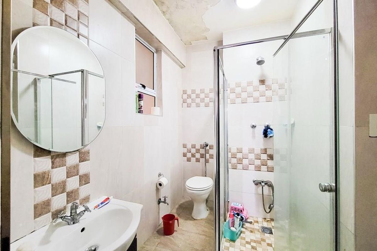 A functional bathroom featuring a shower enclosure, pedestal basin, and toilet, with visible ceiling water damage requiring repair and cosmetic attention.