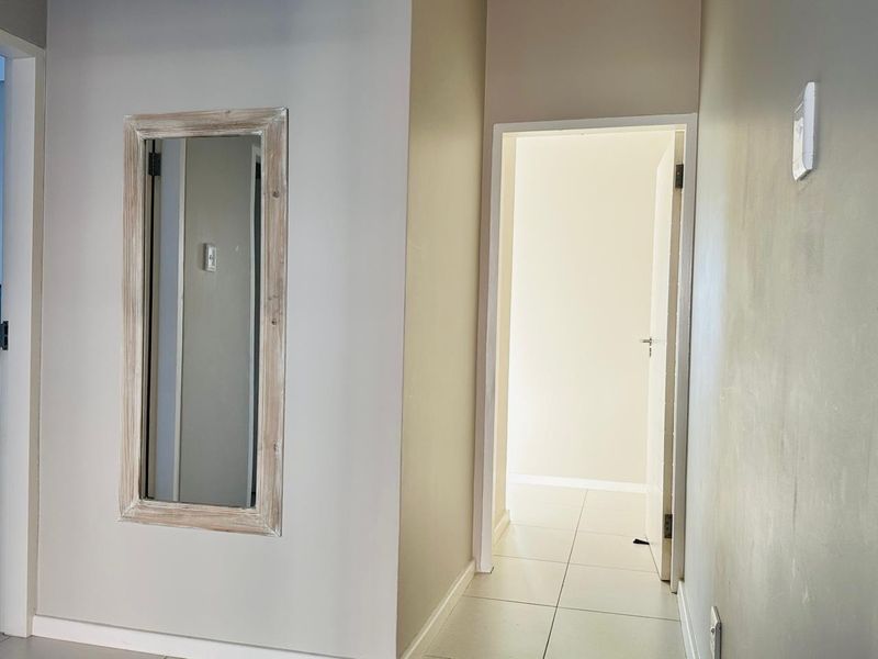 A neutral-toned hallway featuring tiled flooring and a clear transition into an adjacent room.