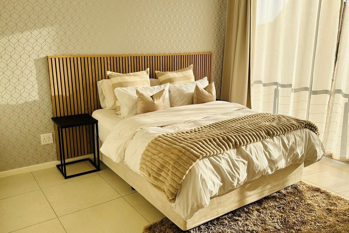 A well-appointed bedroom featuring a modern slatted timber headboard, decorative patterned wallpaper, and neutral tiled flooring with natural light from the adjacent balcony.