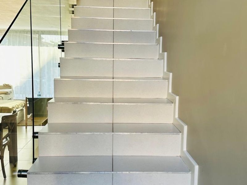 A modern staircase featuring tiled steps and a sleek glass balustrade, leading to an upper level landing.