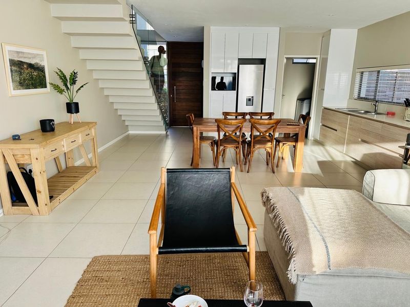 Modern open-plan living area featuring a sleek staircase with glass balustrade, contemporary kitchen cabinetry, and neutral tiled flooring throughout the ground floor.