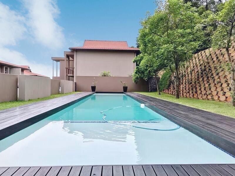 A well-maintained swimming pool area featuring timber decking, a landscaped retaining wall, and a private boundary wall in a townhouse setting.