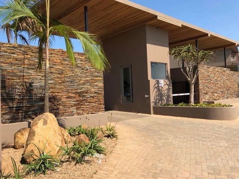 Modern townhouse complex entrance featuring stone cladding, timber ceiling accents, paved driveway, and secure access control point.