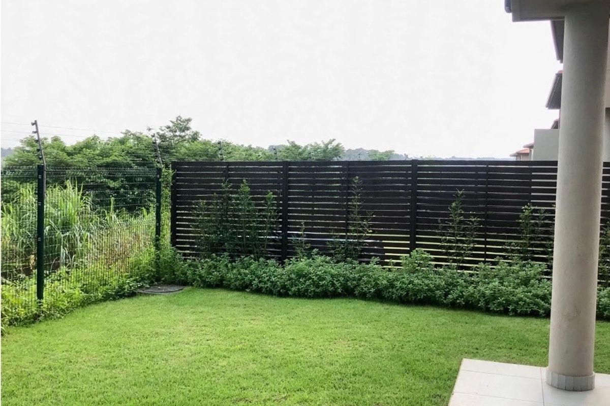 A well-maintained rear garden featuring a tiled patio, concrete column, and privacy screening with secure perimeter fencing.