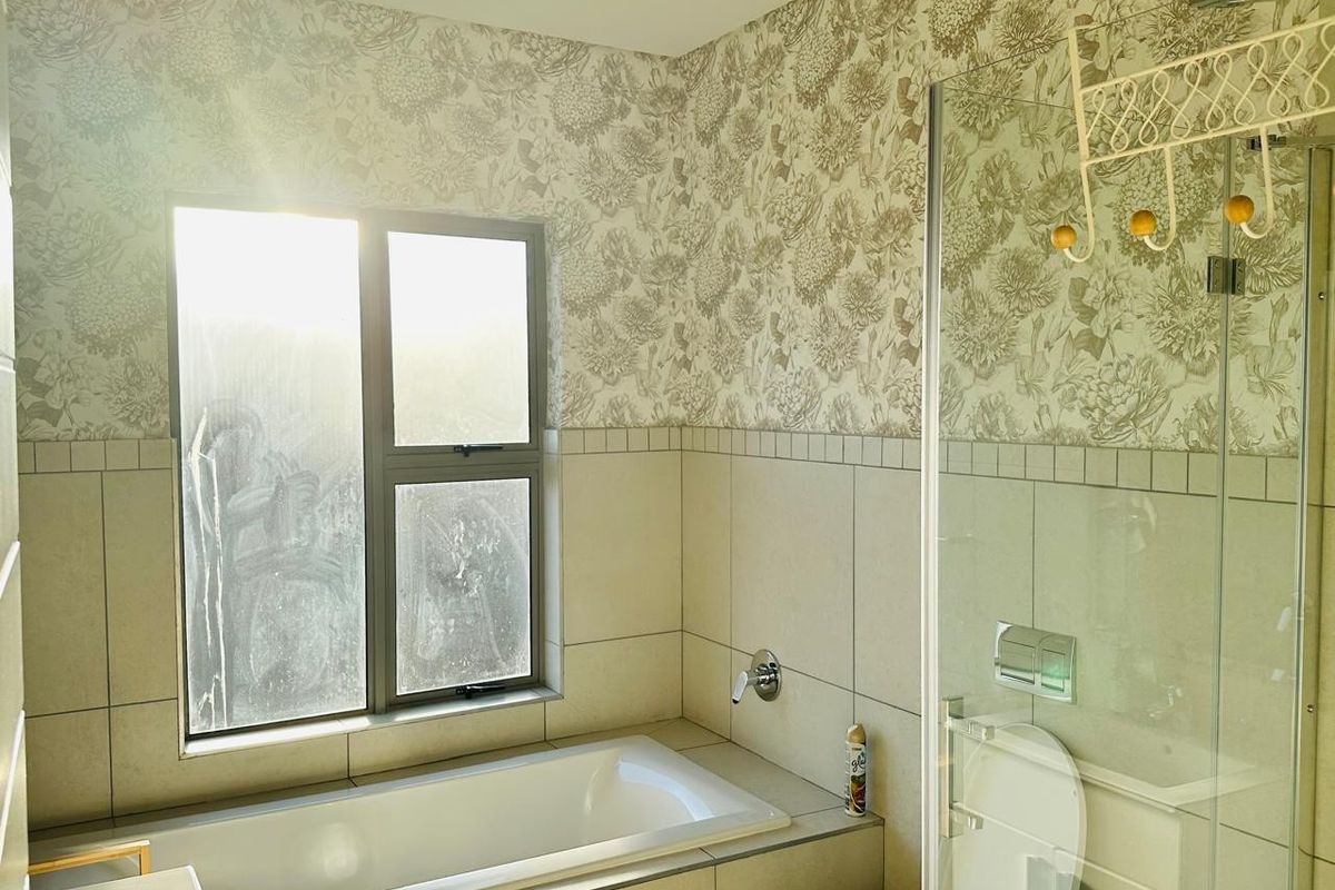 A bathroom featuring a built-in bathtub, glass shower enclosure, tiled walls, and decorative wallpaper, offering a functional space with potential for modern updates.