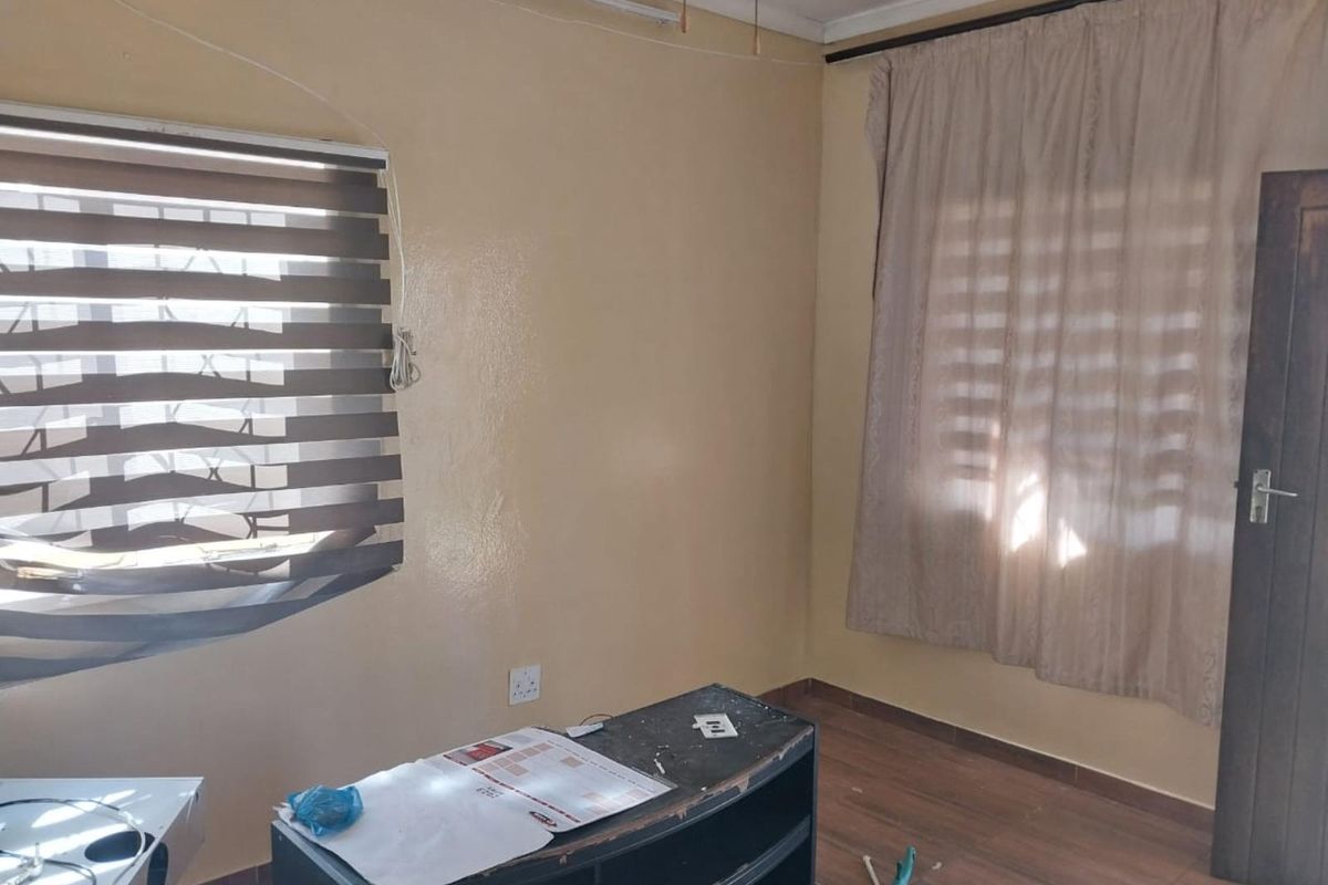 A bedroom featuring wood-look flooring, dual window treatments including zebra blinds and curtains, and a standard wooden door.