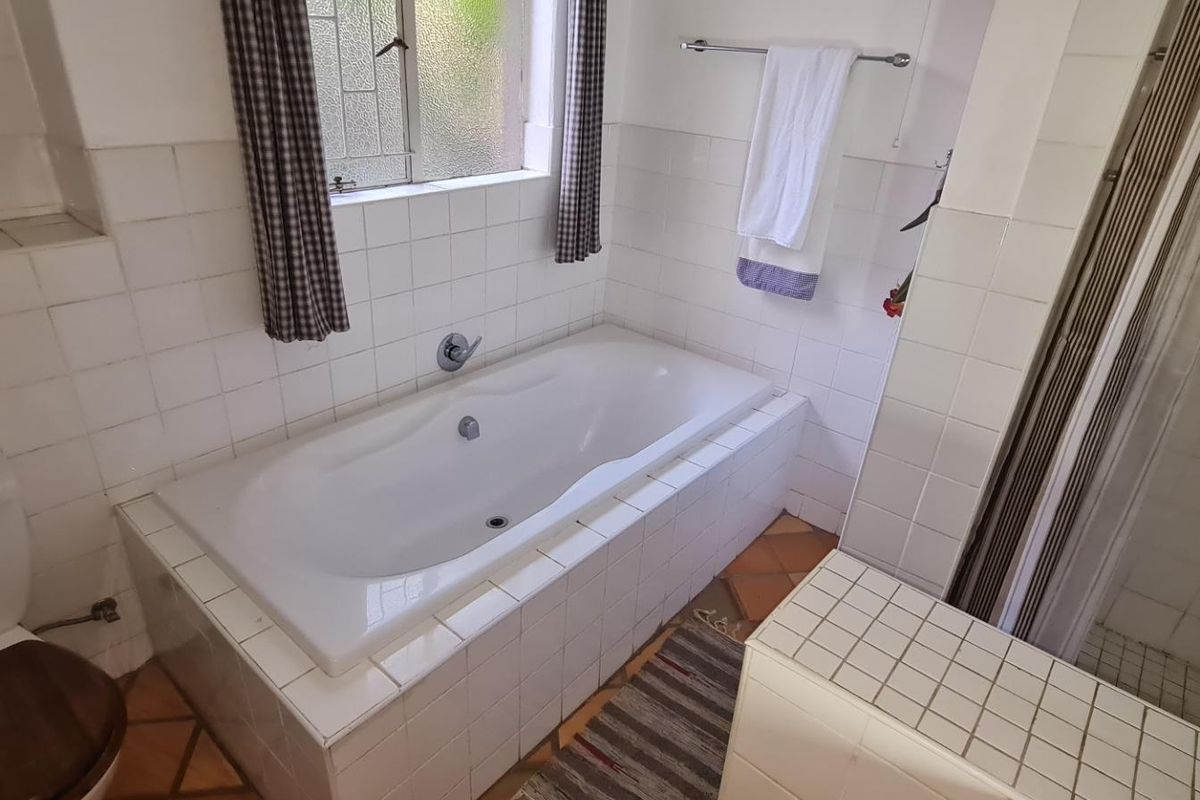A functional bathroom featuring a built-in bathtub, separate shower enclosure, and tiled finishes throughout, offering a classic layout ready for modernization.