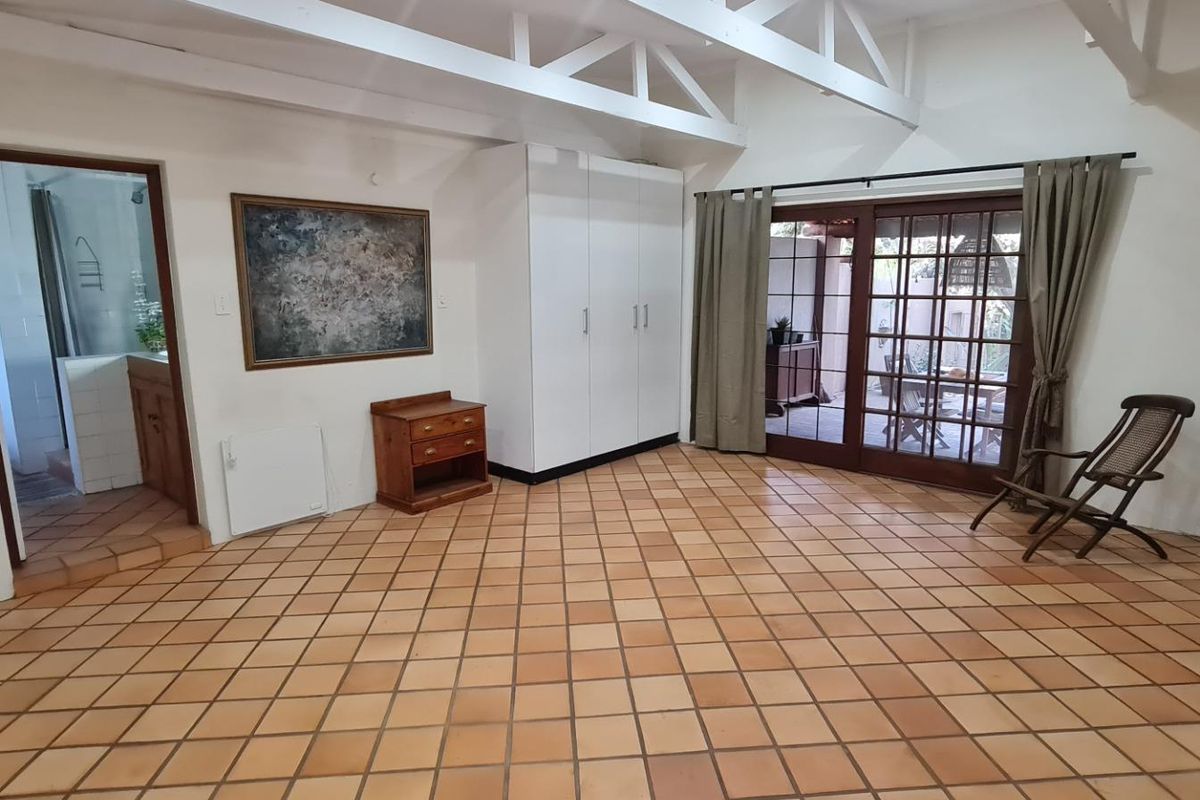 Spacious bedroom featuring exposed timber roof trusses, terracotta tiled flooring, built-in cupboards, and sliding glass doors leading to an outdoor area.