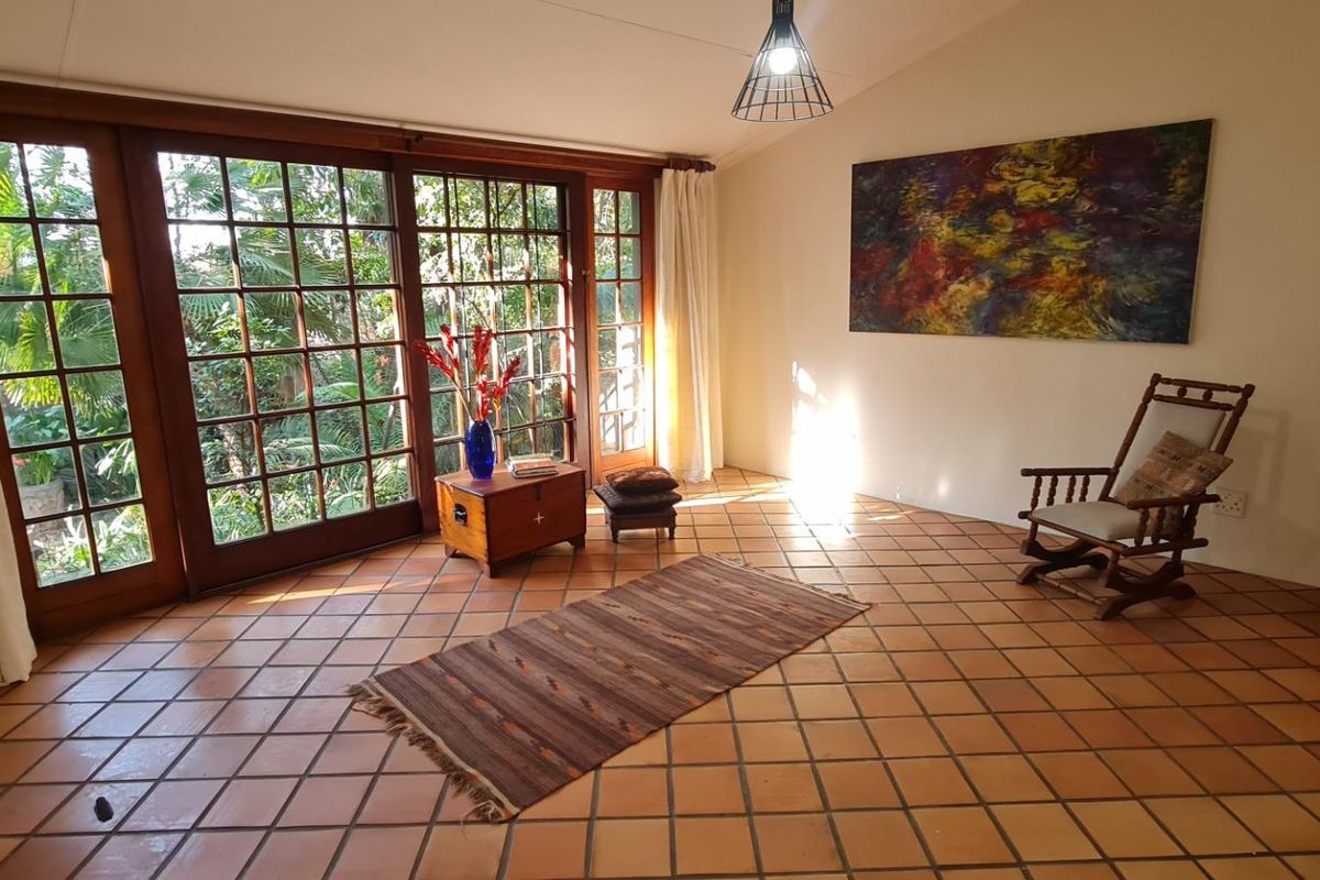 A living room featuring terracotta floor tiles and large timber-framed glass sliding doors that provide natural light and garden views.