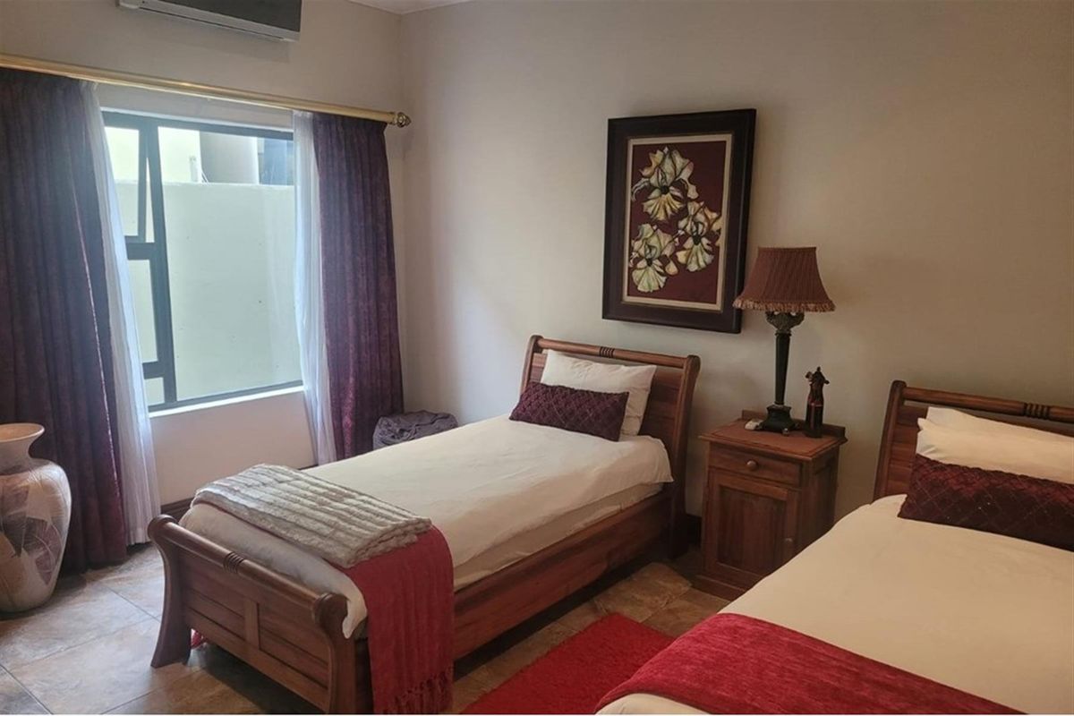 A bedroom featuring tiled flooring, a window with curtain rails, and a wall-mounted air conditioning unit.