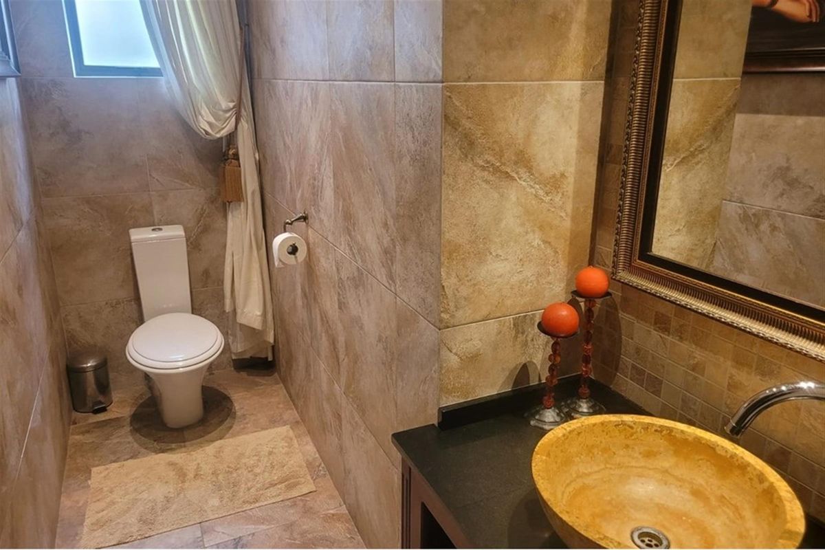 A compact bathroom featuring floor-to-ceiling stone-look tiling, a vessel sink with a dark countertop, and a standard toilet.