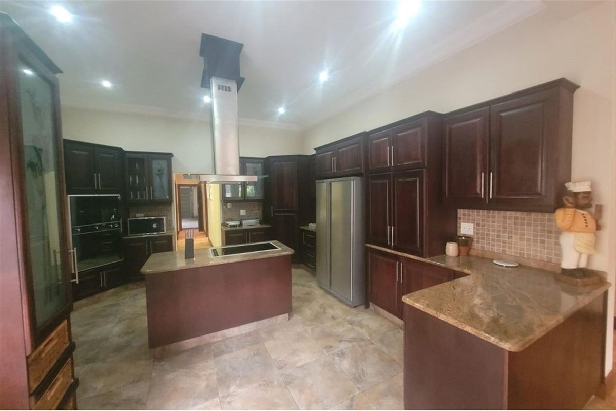 Spacious kitchen featuring dark wood cabinetry, granite countertops, a central island with a built-in cooktop, and a stainless steel extractor fan.