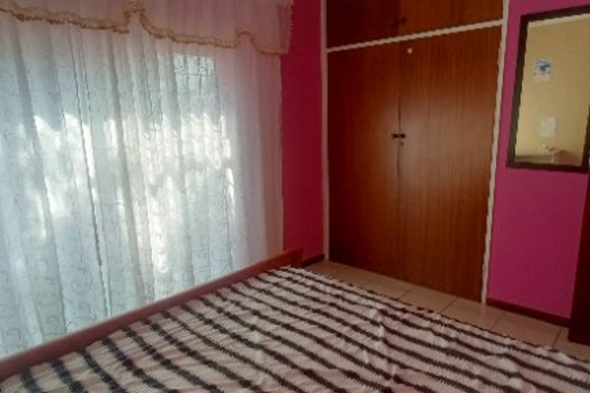 A bedroom featuring built-in wooden cupboards, tiled flooring, and a window with curtains.