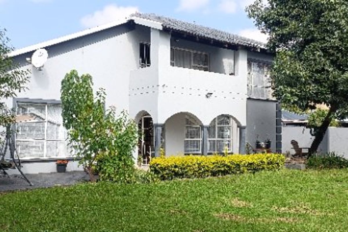 A two-story residential house featuring a rear garden, a covered arched patio, and an upper-level balcony.