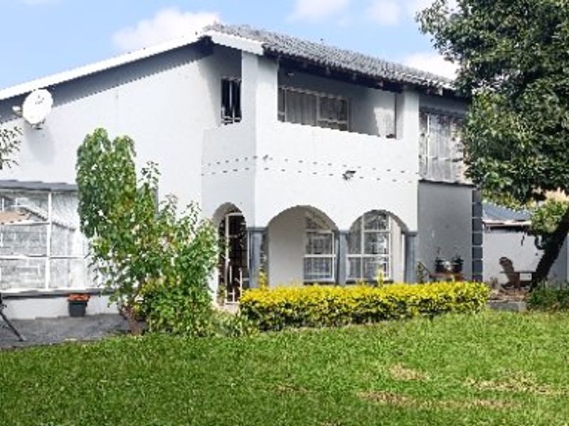 A two-story residential house featuring a rear garden, a covered arched patio, and an upper-level balcony.