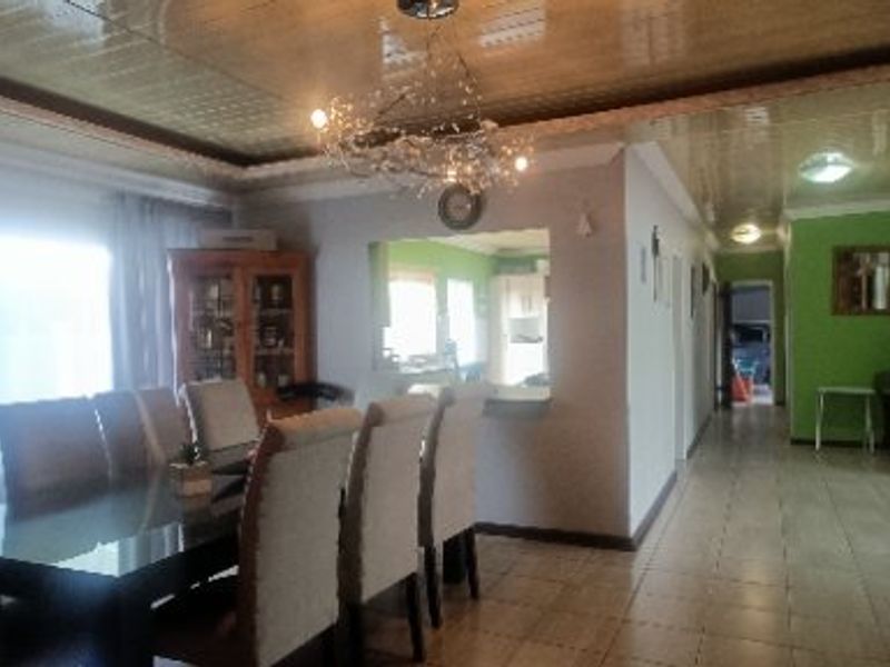 Open-plan dining area featuring tiled flooring and a pass-through window connecting to the kitchen, with a hallway leading to other parts of the home.