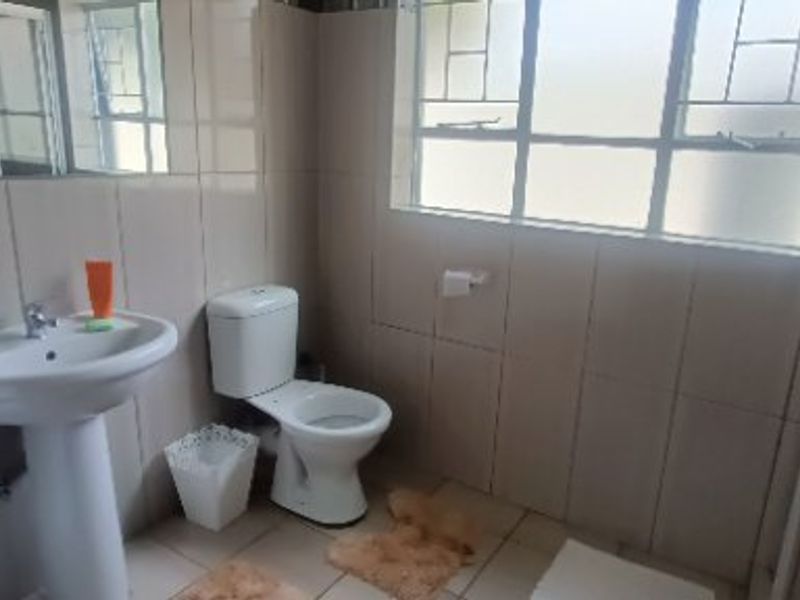 A functional bathroom featuring a pedestal washbasin, toilet, and tiled finishes with natural light from a window.
