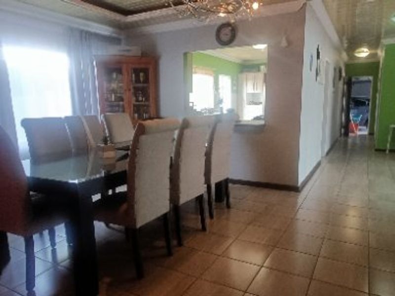 Open plan dining area featuring tiled flooring and a pass-through window connecting to the kitchen, with a view extending into the hallway.