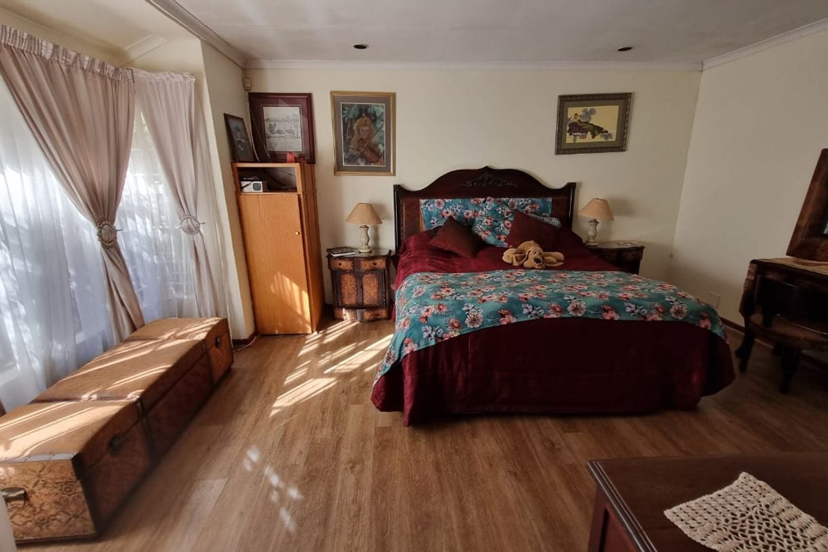 A spacious bedroom featuring wood-look flooring, recessed ceiling lighting, and large windows with curtains, providing a comfortable and well-lit sleeping area.