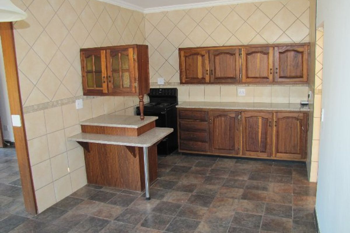 A functional kitchen featuring wooden cabinetry, stone-look countertops, and tiled finishes, offering a blank canvas for potential modern renovation.