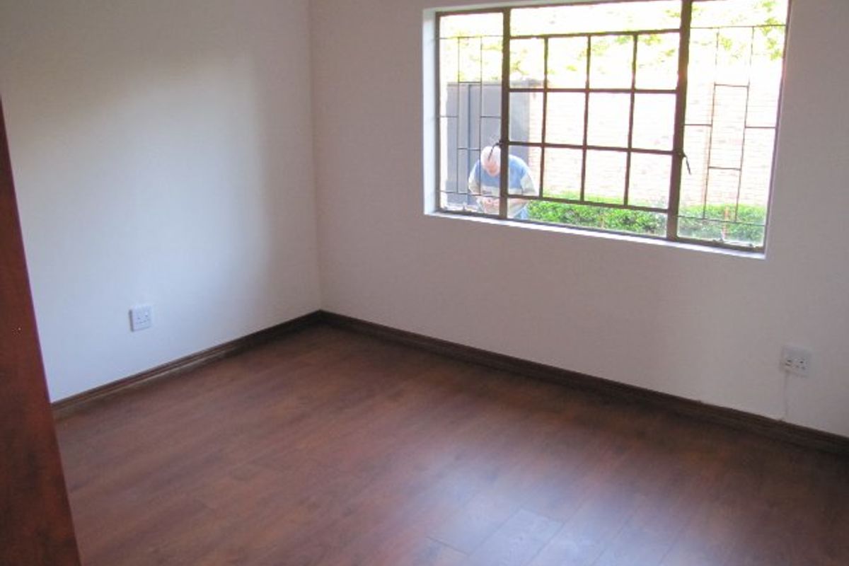 An empty bedroom featuring laminate flooring, neutral walls, and a steel-framed window with security burglar bars.