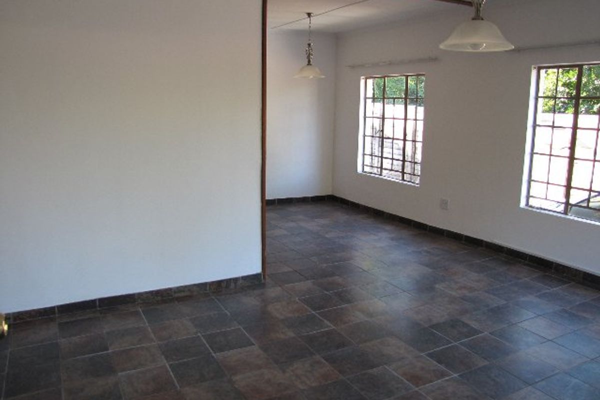 An empty, open-plan living area featuring dark tiled flooring, pendant lighting, and windows fitted with security burglar bars.