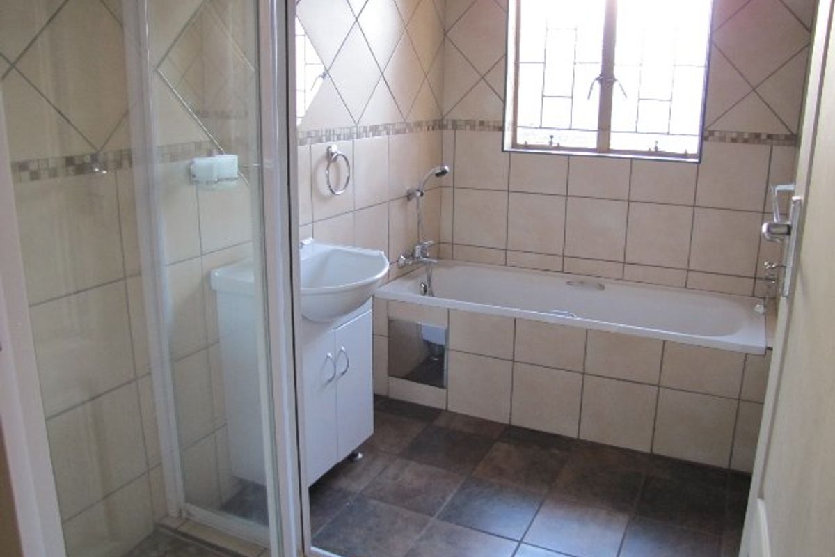 A functional bathroom featuring a separate shower enclosure, bathtub, and vanity basin with neutral tiled finishes and natural light from a window.