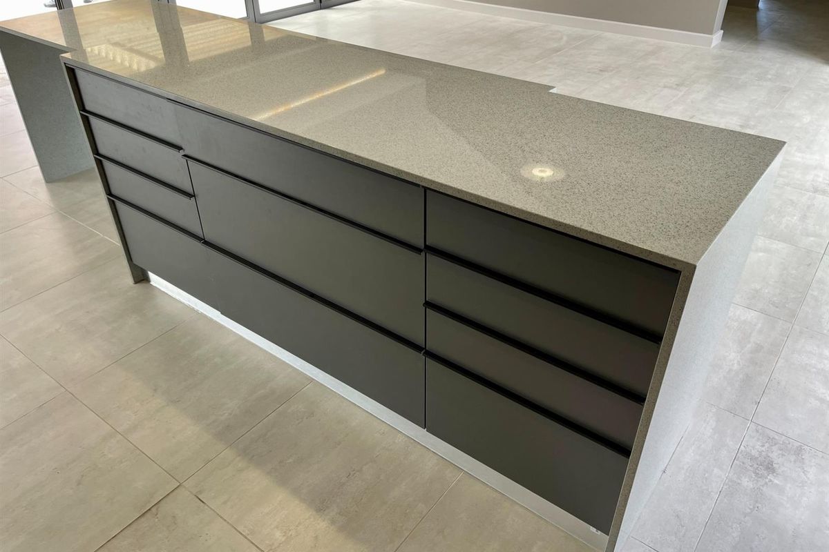 A modern kitchen island featuring sleek handleless cabinetry and a durable stone countertop, set against neutral tiled flooring in an open-plan space.