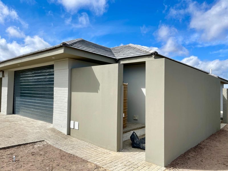 Modern exterior view of a house featuring a roller garage door, tiled roof, and paved driveway with a private side entrance area.