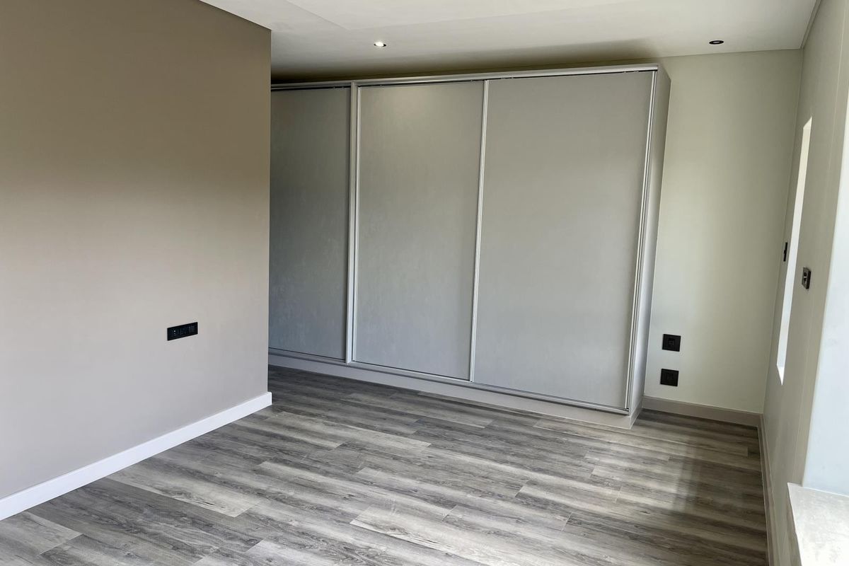 A clean, modern bedroom featuring neutral walls, durable laminate flooring, and extensive built-in cupboard storage with sliding doors.
