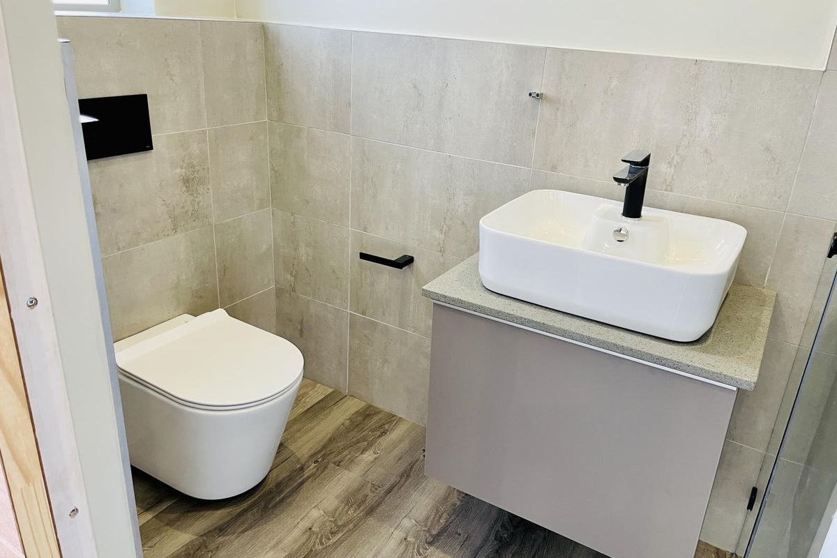 A modern, well-maintained bathroom featuring a wall-hung toilet, vanity cabinet with a countertop basin, and contemporary tiled finishes.