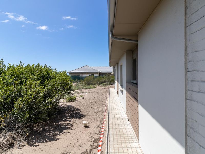 Side view of the property showing a tiled pathway, external wall cladding, and unfinished garden area with sandy ground.