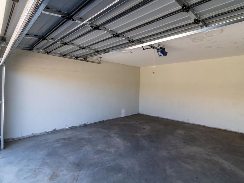 A clean, empty double garage featuring concrete flooring, painted walls, and an automated overhead door mechanism.