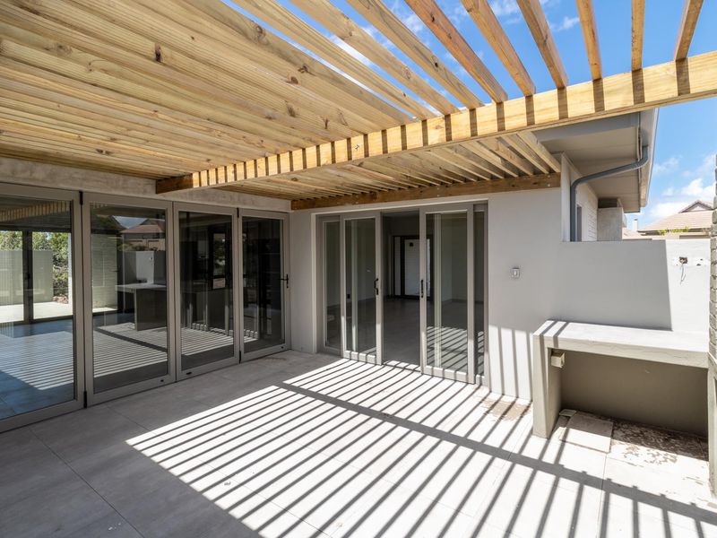 Covered patio area featuring a timber pergola, tiled flooring, built-in braai, and large aluminium stacking doors providing seamless indoor-outdoor flow.