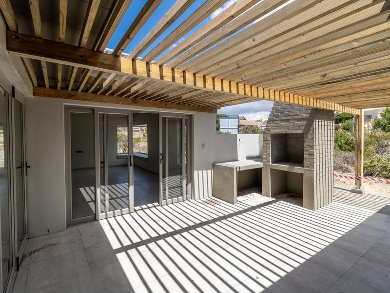 A modern covered patio featuring a timber pergola, built-in brick braai, concrete prep counter, and large sliding glass doors leading to the interior.