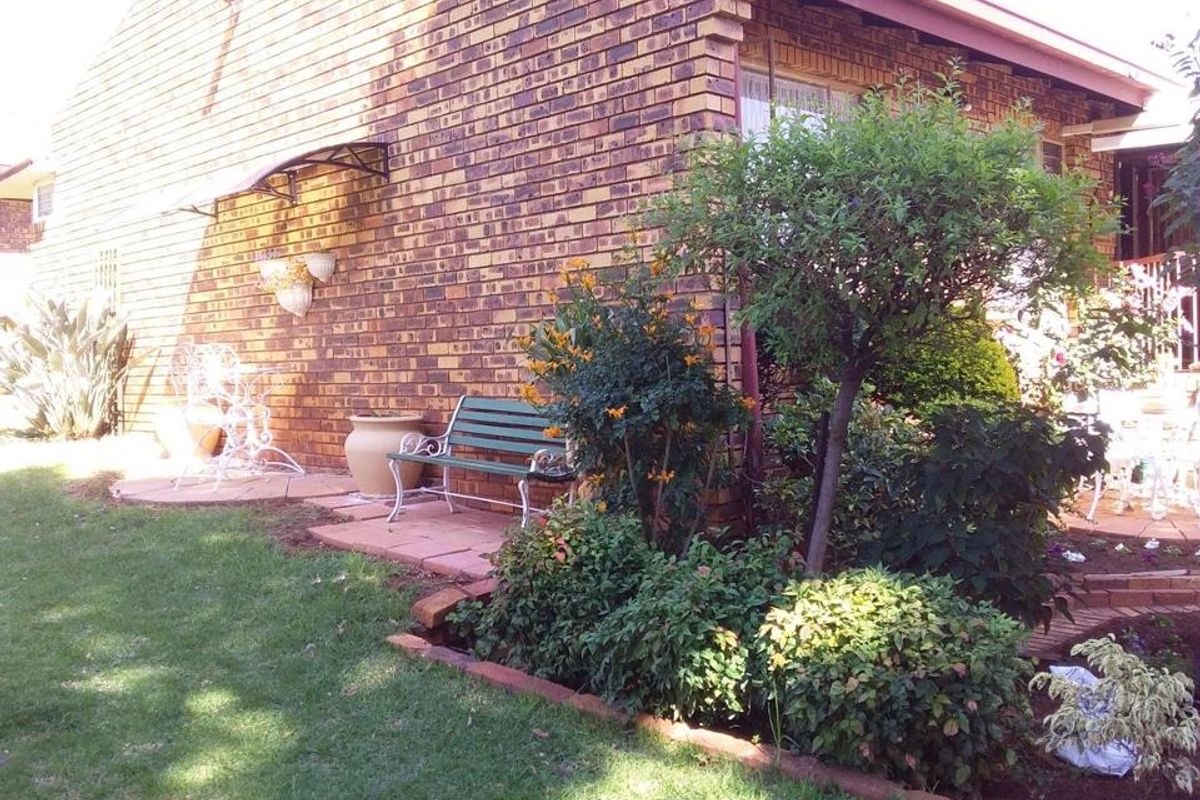 A view of the side garden and brick exterior wall of the retirement village unit, featuring paved areas and established landscaping.