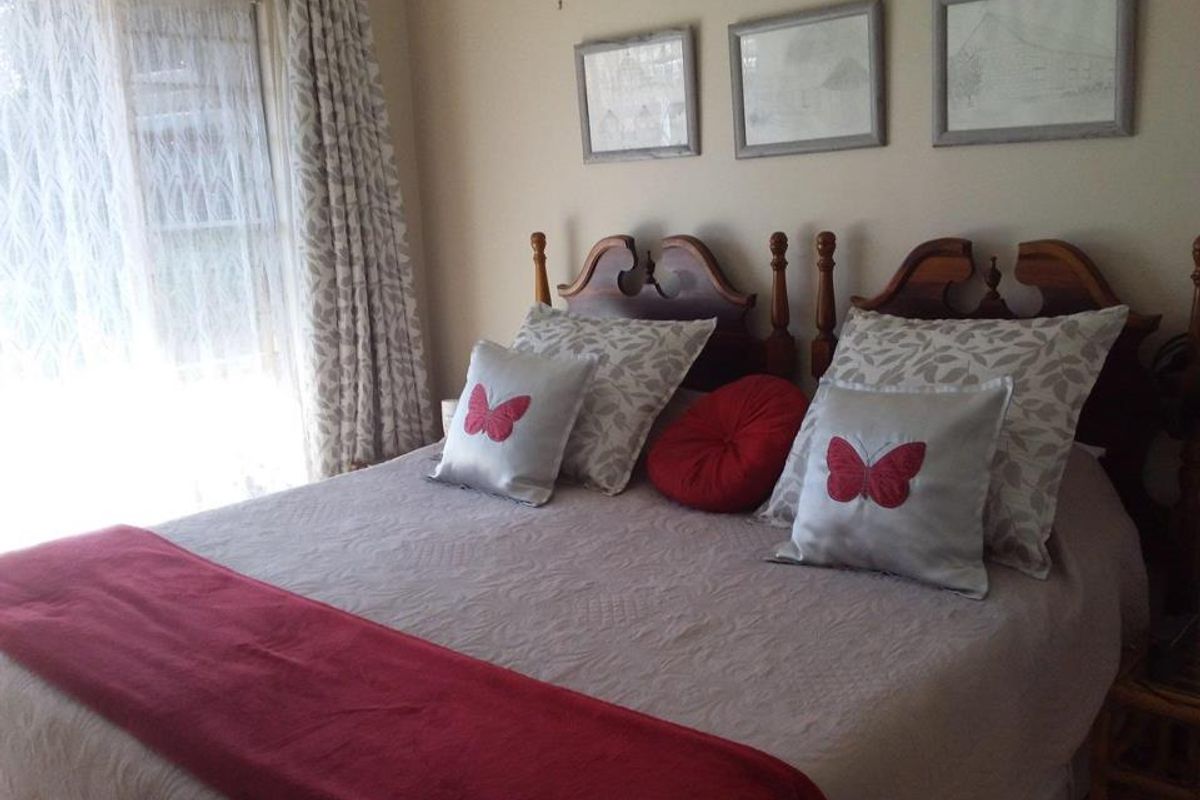 A comfortable bedroom featuring a large window with curtains, providing natural light and a neutral wall finish.