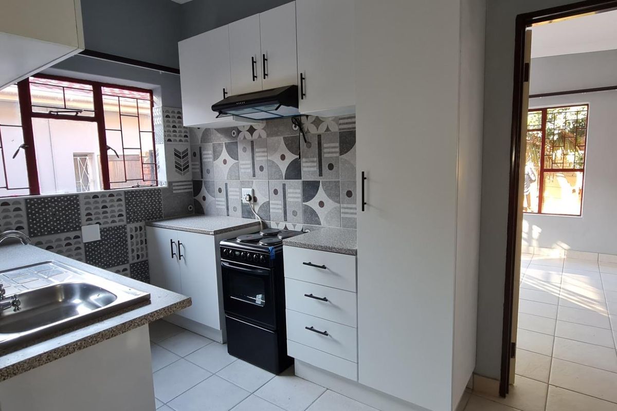 A clean, functional kitchen featuring white cabinetry, patterned tiled backsplash, laminate countertops, and a stainless steel sink with security bars on the windows.