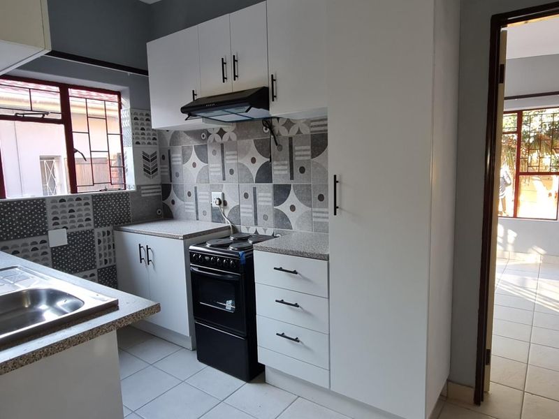 A clean, functional kitchen featuring white cabinetry, patterned tiled backsplash, laminate countertops, and a stainless steel sink with security bars on the windows.