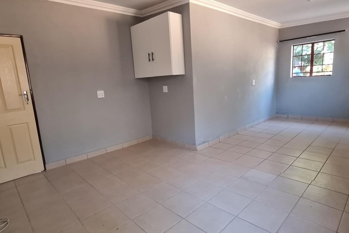 An empty, neutrally painted living area featuring tiled flooring, a wall-mounted storage cabinet, and classic cove cornicing.